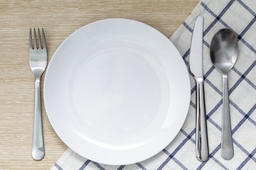 Empty plate with napkin and silverware over wooden table