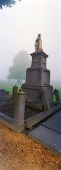 Vertical panoramic view of an old abandoned tombstone in autumnal morning fog