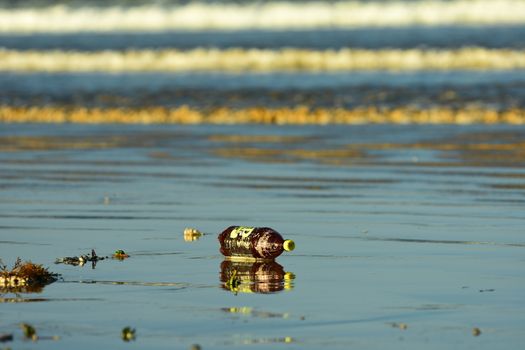 Sea pollution, with a plastic bottle washed ashore on a beach.