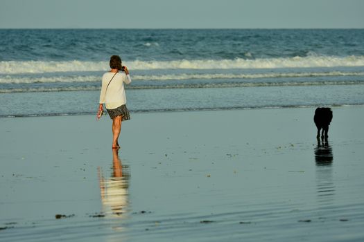 An unidentified young woman enjoying a walk on the beach, with her dog exploring the beach.