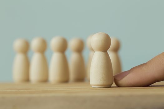 Successful business team leader concept: Hand chooses a wooden figures of man and people standing out from the crowd. depicts human Resource management and recruitment employee or hiring.