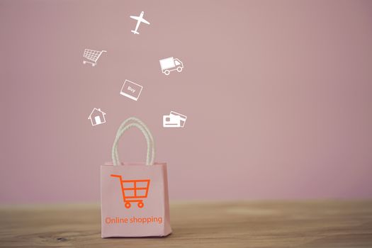 Shopping Online and e-commerce concept: Pink paper shopping bags with shopping cart icon on table. Online stores are considered as another medium of trading goods between entrepreneurs and customers.