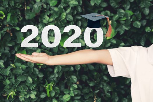 Schoolgirl outstretched arms with Class of 2020 with graduation cap on green nature background