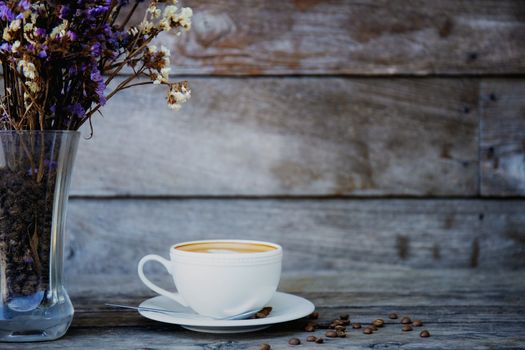 Coffee cup and dry flower in vase on wood with background.