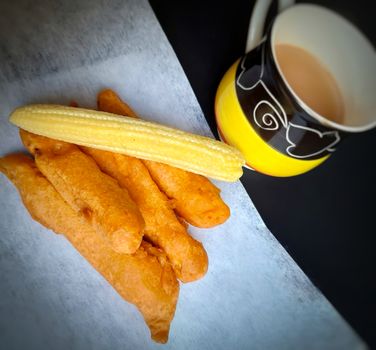 Delicious hot Baby corn baji with fresh baby corn and cup of tea placed in plate with black backgrounds and packed with vital antioxidants and has essential fibres