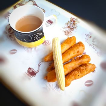 Delicious hot Baby corn baji with fresh baby corn and cup of tea placed in plate with black backgrounds and packed with vital antioxidants and has essential fibres