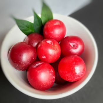 Colorful Red plums kept in bowl with leaves placed in white and black background and reduce the risk of cancer heart disease and diabetes