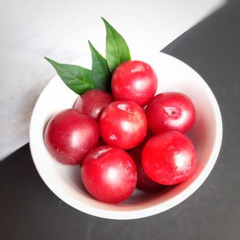 Colorful Red plums kept in bowl with leaves placed in white and black background and reduce the risk of cancer heart disease and diabetes