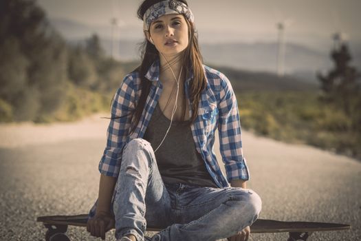 Beautiful young skateboarder girl sitting over her skate