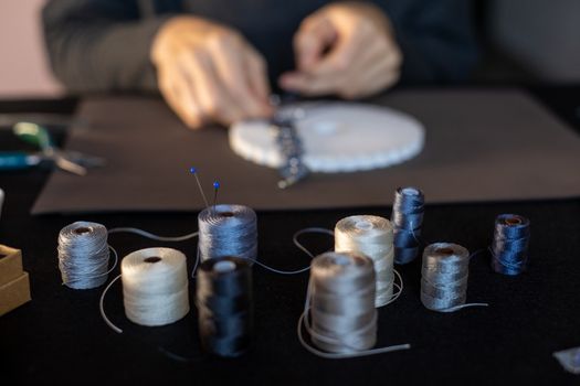 Lifestyle concept, reinvent your life and your job: close-up detail in low angle view of colored spool of thread with the pins threaded on it in foreground with woman hands that knotting the thread