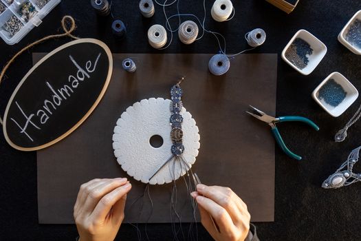 Lifestyle concept, reinvent your life and your job: flat lay top view of woman's hands that knotting a macrame bracelet with tools, spoons and a little blackboard with text handmade chalked