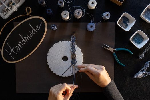 Lifestyle concept, reinvent your life and your job: flat lay top view of woman's hands that knotting a macrame bracelet with tools, spoons and a little blackboard with text handmade chalked