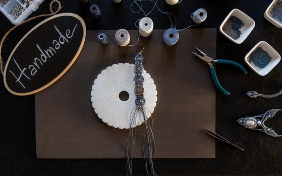 Lifestyle concept, reinvent your life and your job: flat lay top view of macrame jewels with colored spools of thread, a bracelet, beads, tools and a little blackboard with text handmade chalked