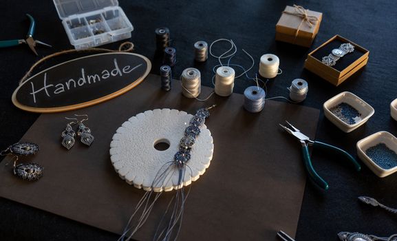 Lifestyle concept, reinvent your life and your job: angle top view of macrame jewels with colored spools of thread, a bracelet, beads, tools and a little blackboard with text handmade chalked