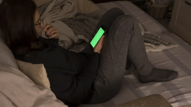 Couple relationships and dating in modern times concept: closeup of woman sitting on her sofa using her smartphone with blank green screen in low light