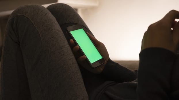 Couple relationships and dating in modern times concept: closeup of woman sitting on her sofa using her smartphone with blank green screen in low light