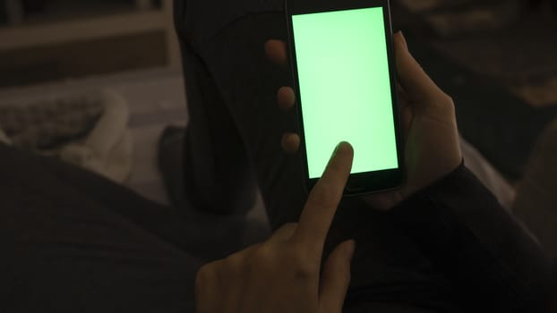 Couple relationships and dating in modern times concept: closeup of woman sitting on her sofa using her smartphone with blank green screen in low light