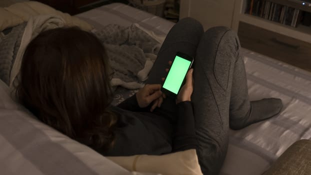 Couple relationships and dating in modern times concept: closeup of woman sitting on her sofa using her smartphone with blank green screen in low light