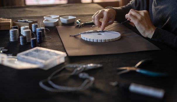 Lifestyle concept, reinvent your life and your job: close-up detail in low angle view of woman hands making macrame knotted bracelet with the fingers knotting the nylon thread on the kumihimo