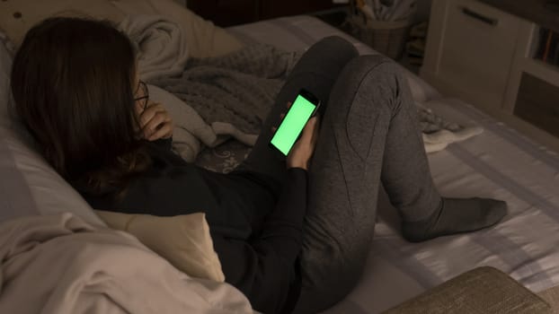 Couple relationships and dating in modern times concept: closeup of woman sitting on her sofa using her smartphone with blank green screen in low light