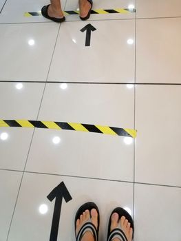 People stand in yellow black footprint  line on the floor of the store to maintain social distance. Concept of the coronavirus pandemic and prevention measures.