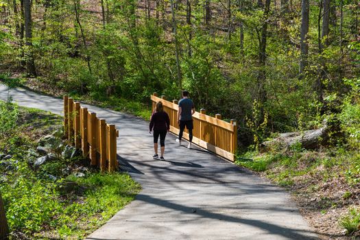 Reston, VA, USA -- April 21, 2020. Photo of a man and woman walking over a bridge on a hiking trail around Lake Audubon in in Reston, VA