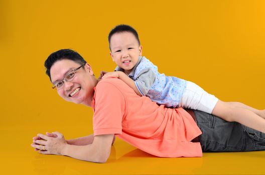 Happy father's day! joyful young dad  playing with  his cute son. Father giving young boy piggyback ride on floor at home. Isolated on orange background.