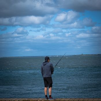 Barnegat, NJ, USA -- September 13, 2019. Photo of a young man fishing in Barnegat Bay from the boardwalk in Barnegat, NJ.