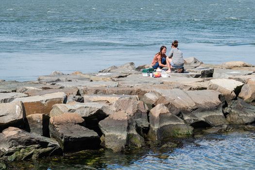 Barnaget, NJ, USA -- September 13, 2019. Photo of two young women fishing from a stone jetty in Barnaget Bay, NJ.