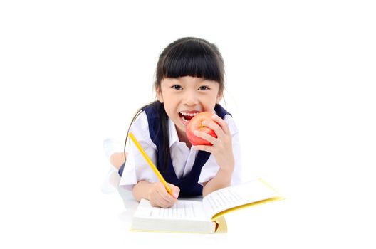 Back to school. Portrait of happy asian cute little child girl in uniform writting on the book, lying down on the floor, isolated over white  background.