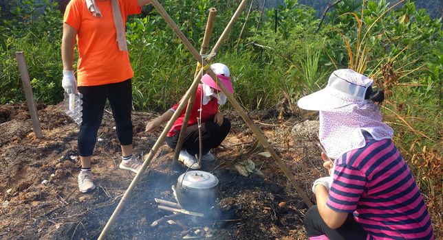 Group of asian hiking girl cooking in a black pot on around a bonfire at outdoor forest.