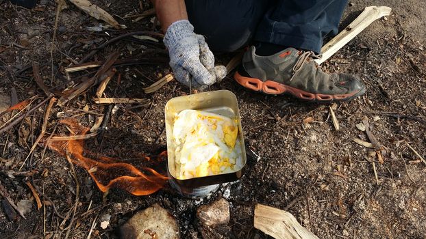 person cooking fried eggs in nature camping outdoor, cooker prepare breakfast scrambled picnic on metal pan.