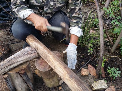 A man hammer a tree with a hammer and  nail for making a chair at garden.