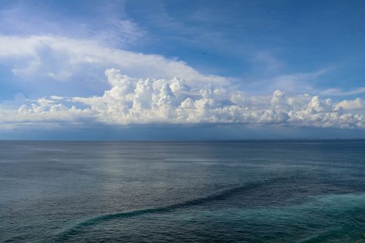 Calm sea and blue sky from the side of a boat with bow wave wake and cumulonimbus clouds on the horizon