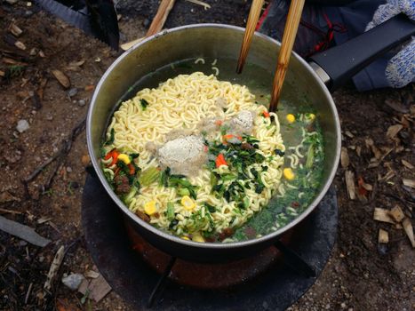 Cooking instant nodles at outdoors in black pot at picnic on fire.