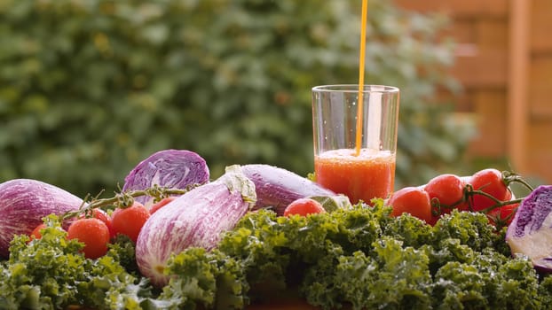 Close up tomato juice pouring into a glass, fresh vegetables on the table in drops of water. Harvesting in a country farm. Healthy food concept