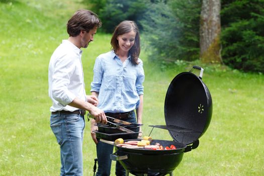 Couple cooking food corn vegetables sausage on barbecue grill at backyard