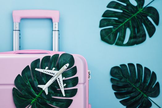 White airplane model on pink luggage with palm leaves on blue pastel colored background travelling and summer beach concept