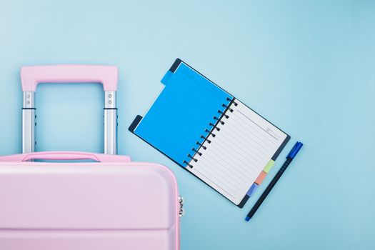 Pink luggage with a checklist diary on blue background for travel planning concept