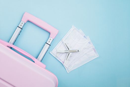 Pink luggage with white airplane model and hygiene face mask on blue background for travelling and new normal or new way of living concept