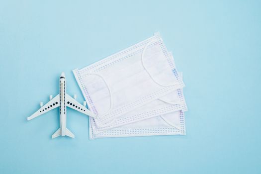 White airplane model with hygiene face mask on blue background for travelling and healthcares concept