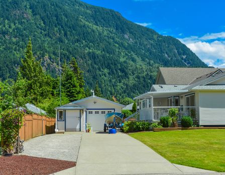 Suburban family house with mountain view and blue sky background. Residential house with garage on the back yard and small boat parked on concrete driveway.