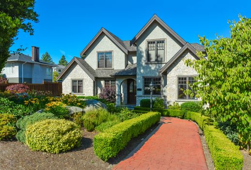 Luxury residential house with red paved pathway to the entrance on blue sky background