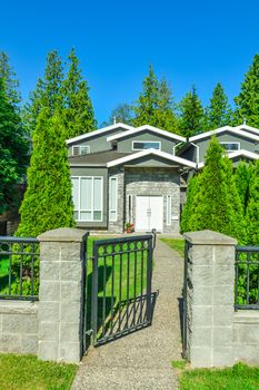 Main entrance of residential duplex house with open metal gate in front. Family home with concrete pathway over the front yard on bright sunny day