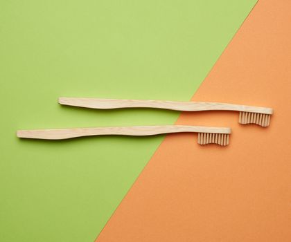 two wooden toothbrushes on a green orange background, plastic rejection concept, zero waste 