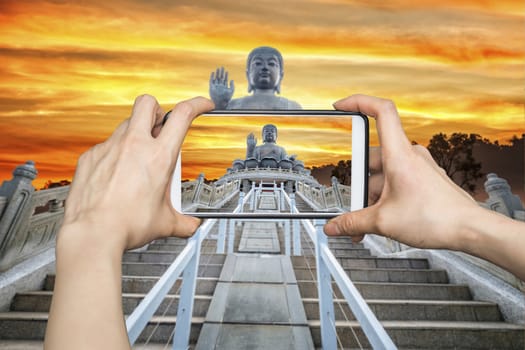 Girl taking pictures on mobile smart phone in Front View of Tian Tan Giant Buddha in golden sky