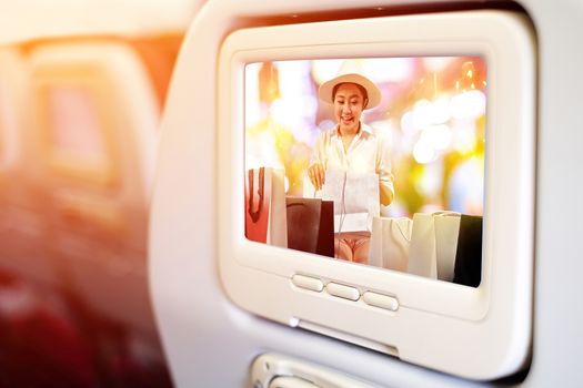 Aircraft monitor in front of passenger seat showing a happy shopaholic women opening a shopping bag