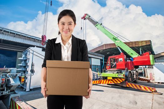 A young woman carrying a box wtih smile in construction site background

