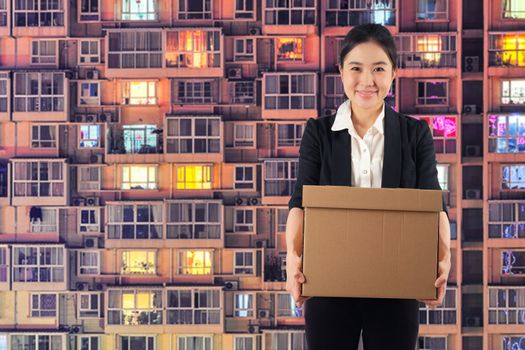 A young woman carrying a box wtih smiling on Condominium background

