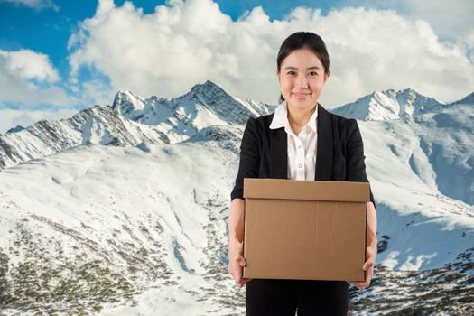 A young woman carrying a box wtih smiling on snowmoutain background

